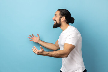 Welcome, wide open hug. Side view of man with beard wearing white T-shirt stretching hands to...