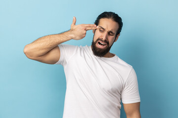 Portrait of frustrated desperate man with beard wearing white T-shirt pointing finger gun to head,...