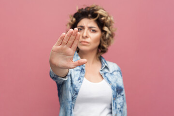 Portrait of strict bossy woman with curly hairstyle wearing blue shirt standing showing stop...