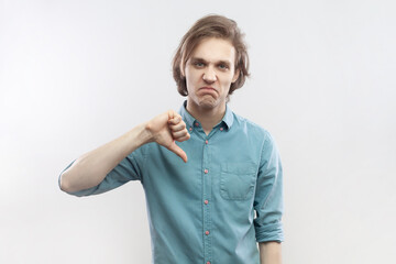 Portrait of young man criticizing bad quality with thumbs down displeased grimace, showing dislike...