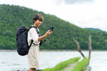 Asian non binary people relax and enjoy outdoor lifestyle travel forest mountain on summer holiday vacation. Generation z LGBTQ person using mobile phone taking selfie with beautiful nature at lake.