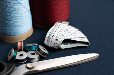 measuring tape, cones of threads with metal scissors on blue fabric