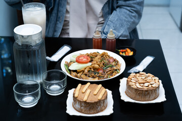 A photo of a hand enjoying a meal with a menu of Kwetiaw noodles, ice cream, water, and a milkshake on the table