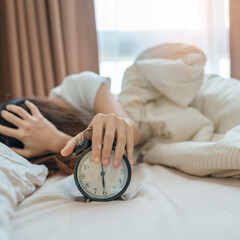 alarm clock and asian woman hand stop time in bed while sleeping, young adult female wake up late...