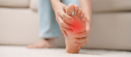 woman having barefoot pain during sitting on couch at home. Foot ache due to Plantar fasciitis and...