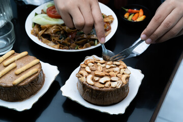 A photo of a hand enjoying a meal with a menu of Kwetiaw noodles, ice cream, water, and a milkshake on the table