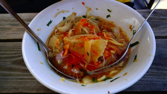 eat a bowl of meatball sauce mixed with spicy chili sauce using a spoon and fork