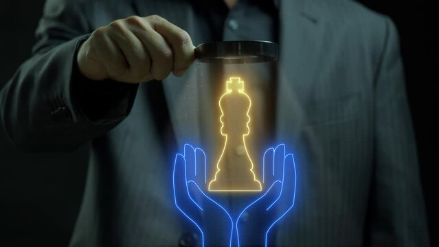 Business man holding a magnifying glass that showing an animation king chess showing on human palm. Concept for teamwork, hiring, human resource management or leadership.
