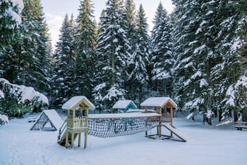Wooden snow-covered playground in a coniferous forest