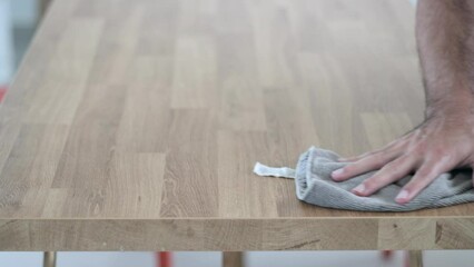 Person cleaning a wooden table surface with a cloth. Close-up of hand wiping