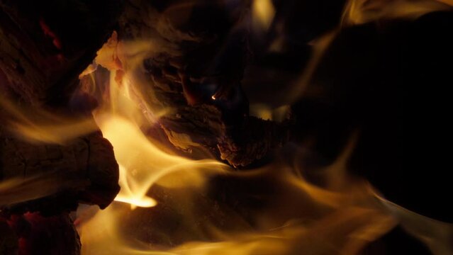 Vertical shot of burning firewood in bonfire. Closeup of glowing embers and sparks in dark. Wooden logs smoldering in fire. Fire flames moving on black background. Camfire in forest, 4k footage