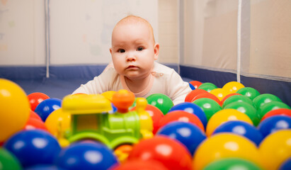 Cute baby girl playing with colorful balls in kindergarten.