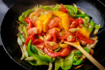 Stir-fried tomatoes and bell peppers in an iron pan.