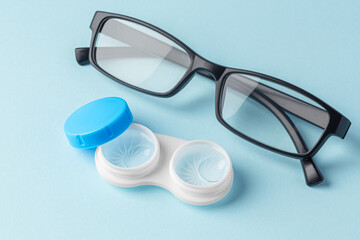 Fototapeta na wymiar Contact lenses in case with solution liquid with eyeglasses on light blue background