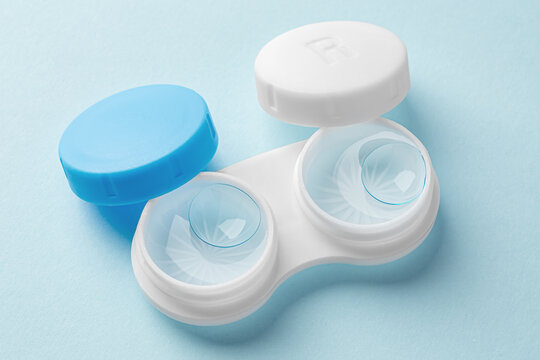 Contact lenses in case with solution liquid on light blue background