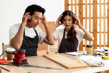 Two carpenters wearing safety headsets while woodworking in workshop, protect hearing using ear...