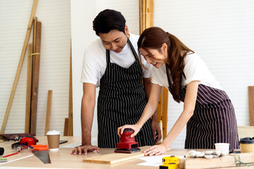 Workshop Learning: A Carpenter Guides a Woman in Using an Electric Sander for Woodwork Projects - 702048110