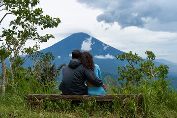 A couple of lovers are sitting on a bench, hugging each other and enjoying the view of the popular...