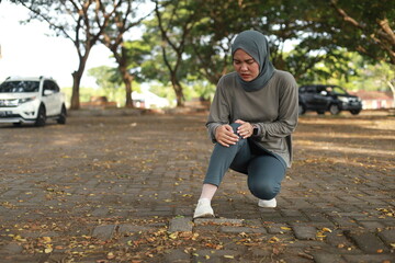 Joint pain, Arthritis and tendon problems. an asian muslim woman touching knee at pain point in the park.