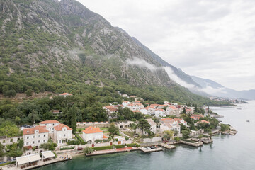 Fototapeta na wymiar Ancient houses with red roofs at the foot of the mountains on the shores of the Bay of Kotor. Dobrota, Montenegro. Drone