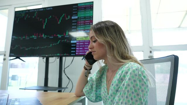 Sad clerk Blonde European woman working at the office financial trading. Background trading view Bitcoin and stock market. Business phone call. Business woman entrepreneur talking by phone.