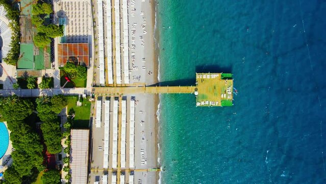 Aerial 4K drone wide top down video of a wooden pier near hotel resort in the city of Kiriş - Kemer (Antalya, Turkey). Filmed in a vibrant summer time. Mediterranean sea.