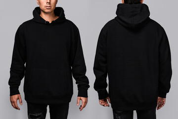 Front and back views of a man wearing a black, oversized hoodie with blank space, ideal for a mockup, set against gray background - obrazy, fototapety, plakaty