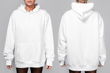 Front and back views of a woman wearing a white, oversized hoodie with blank space, ideal for a mockup, set against gray background