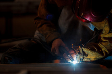 Heavy industry duty worker using a welding torch welds an iron steel in factory.