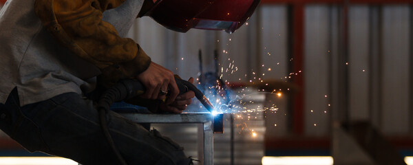 Heavy industry duty worker using a welding torch welds an iron steel in factory.