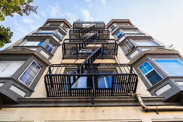 Exterior view of multifamily residential building; Old metal fire escape stairs hanging on side of the building; Berkeley, San Francisco Bay Area, California - obrazy, fototapety, plakaty
