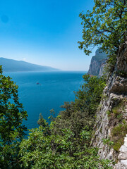 Fototapeta na wymiar View of Lake Garda towards the south. In the background the ridges of Monte Baldo. In the foreground the rocks of Tremosine.