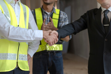 Engineer shaking hands at construction site with happy architect.