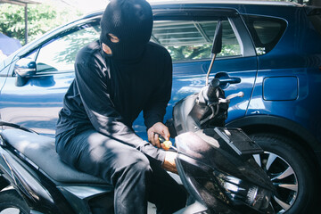 Motorcycle thief in black mask using screwdriver to tamper motorcycle locks 
