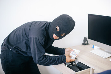 Masked burglar stealing money from drawer after breaking into a house