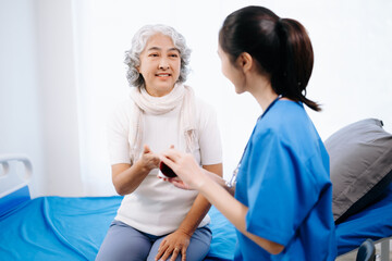 Doctor in white suit take notes while discussing and Asian elderly, woman patient who lying on bed with receiving saline solution