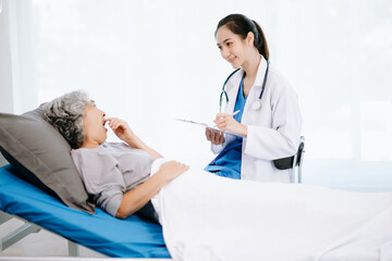 Fototapeta premium Doctor in white suit take notes while discussing and Asian elderly, woman patient who lying on bed with receiving saline solution