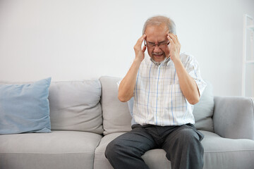 senior asian man suffering from headache on sofa