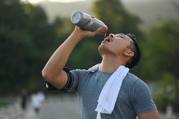 Handsome athletic male drinking water from bottle after running resting after workout outdoors.