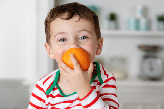 Happy little boy biting in an orange