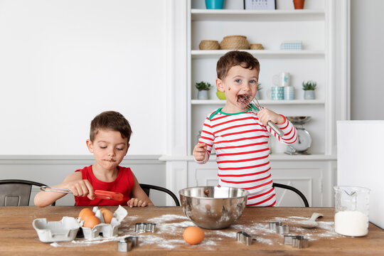 Young boys with messy chocolate face baking at kitchen table