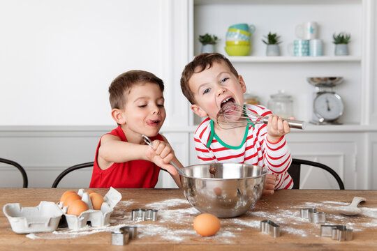 Funny siblings with messy face licking chocolate out of mixing bowl while baking