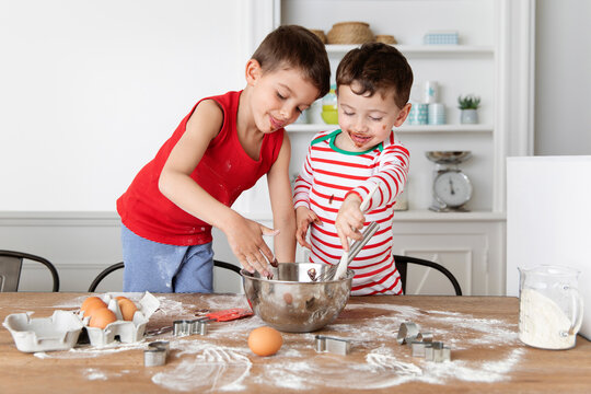 Happy siblings with messy face and clothes baking chocolate cake together