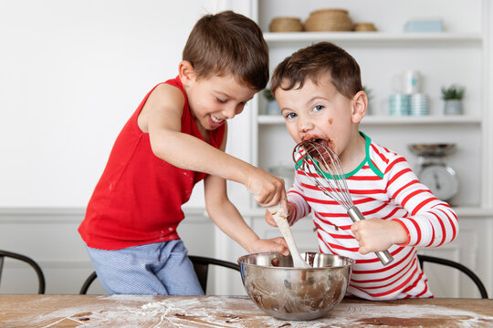 Funny brothers with messy face licking chocolate out of mixing bowl while baking
