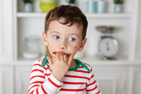 Young boy with messy chocolate face licking his fingers