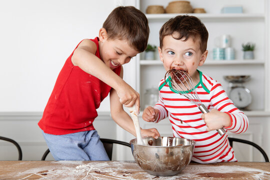 Funny young boys with messy face licking chocolate out of mixing bowl while baking