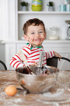 Smiling young boy with messy face baking chocolate cake at kitchen table