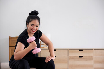 Fototapeta na wymiar Fat woman exercising at home A beautiful oversized woman in a sports bra and casual pants sits in the living room and exercises with dumbbells.