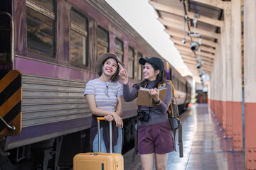 Two Asian female tourist friends are at the train station. Waiting for the train to travel to the provinces together on the weekend.