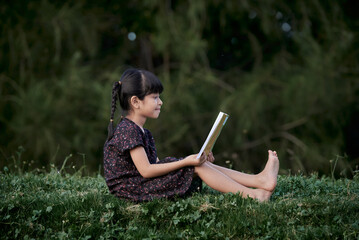 Little girl sits and reading a book in the green rainforest